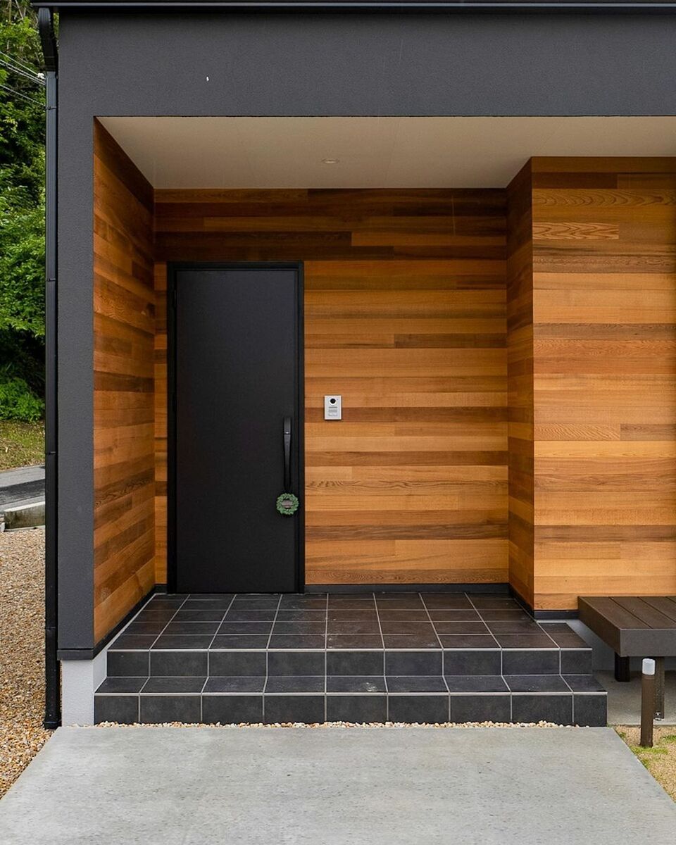 木目の美しいラグジュアリーな玄関ポーチはブラックのドアが空間を引き締めます