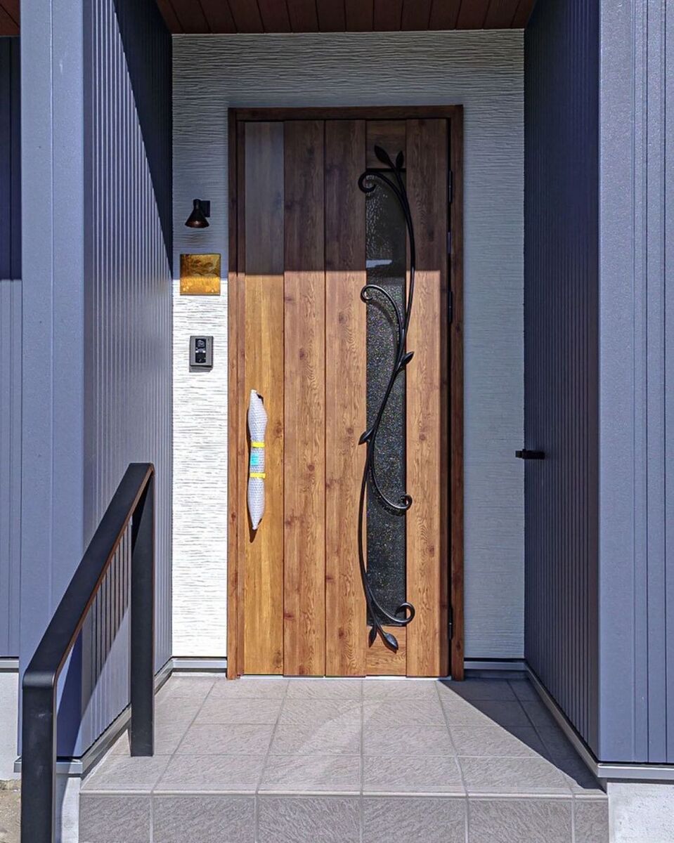 玄関前には木製ドアのおしゃれなアイアン飾りに揃えてアイアンの手すりを設置