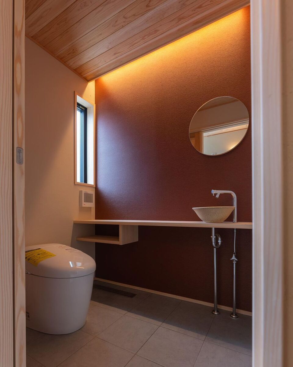 トイレにもあずき色のアクセントクロスと丸い鏡、陶器の洗面ボールで和モダンスタイル