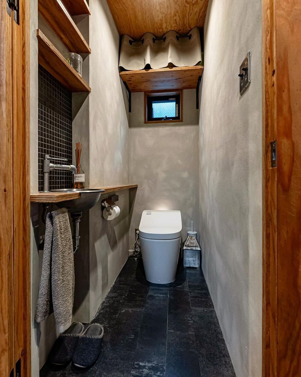 トイレはモルタル＋ブラックタイルのモノトーンベースの無機質な空間に無垢材の温かみが加わったナチュラルモダンな落ち着く空間
