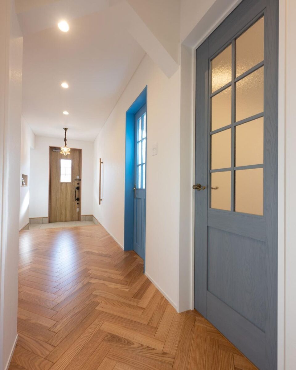 ヘリンボーン柄のフローリングにブルーのグラデーションがおしゃれな室内ドア、アンティーク調のペンダントライトが可愛い素敵な玄関ホール