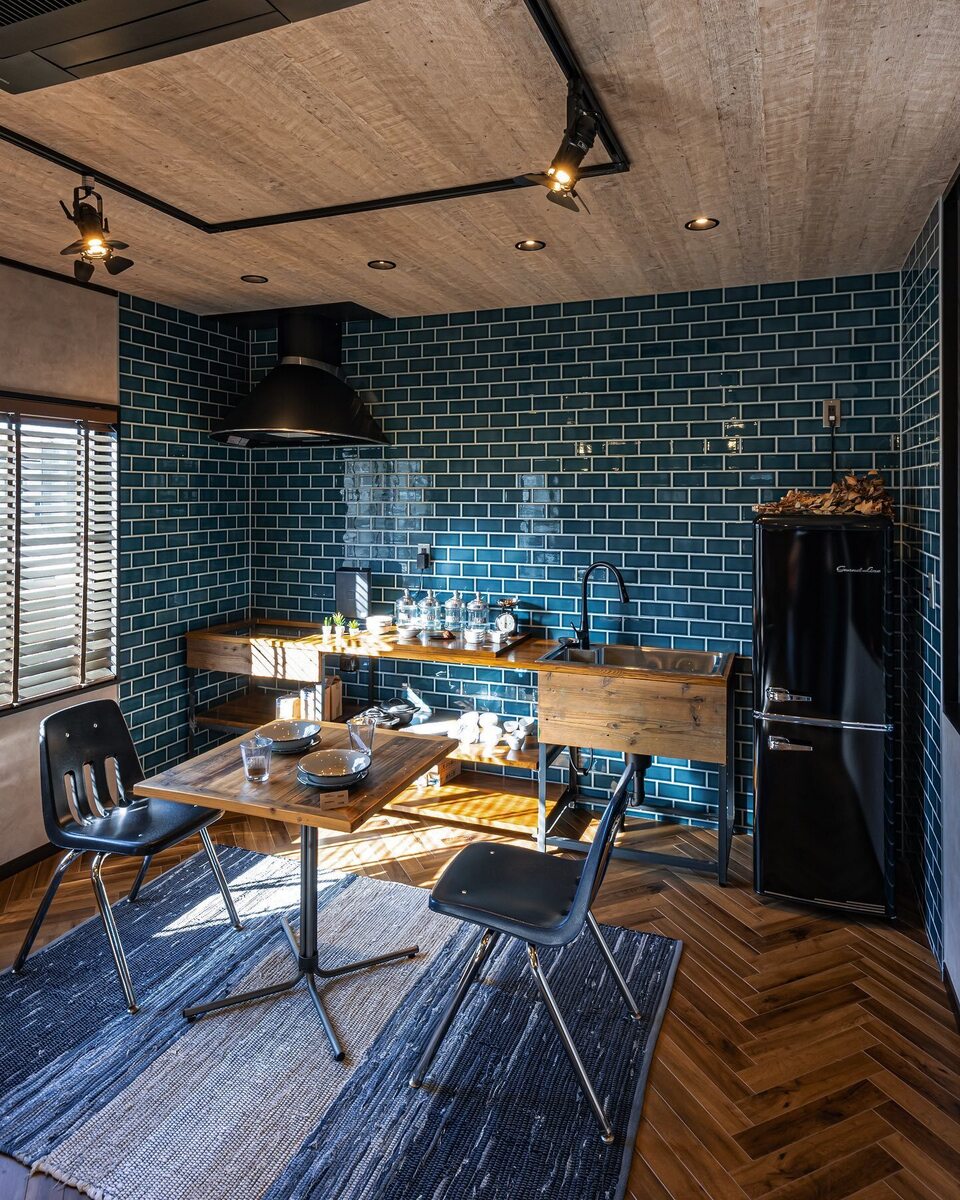 キッチンを囲んでコの字に貼られたブルーグリーンのサブウェイタイルが目を引くおしゃれなダイニングキッチン。木×アイアンの造作キッチンやへリンボーン柄の床、ブラックのスポットライトがインダストリアルでかっこいい空間に！