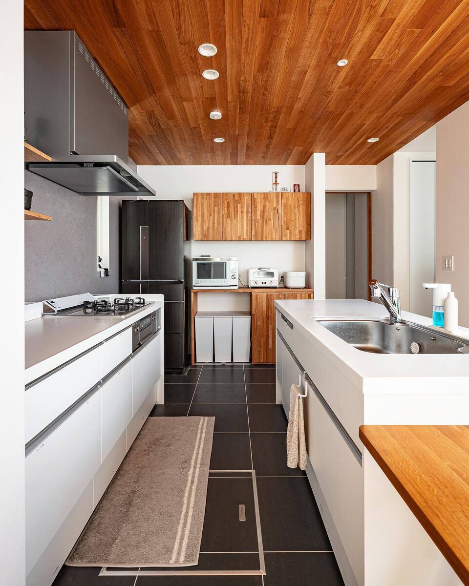 シンクとコンロが別々になったⅡ型キッチンは作業スペースも広く機能的◎白いキッチン、グレーのアクセントクロス、お手入れしやすくカッコいいダークグレイのタイルの床とスタイリッシュモダンな空間に木目の天井とカップボードで柔らかさをプラス✨