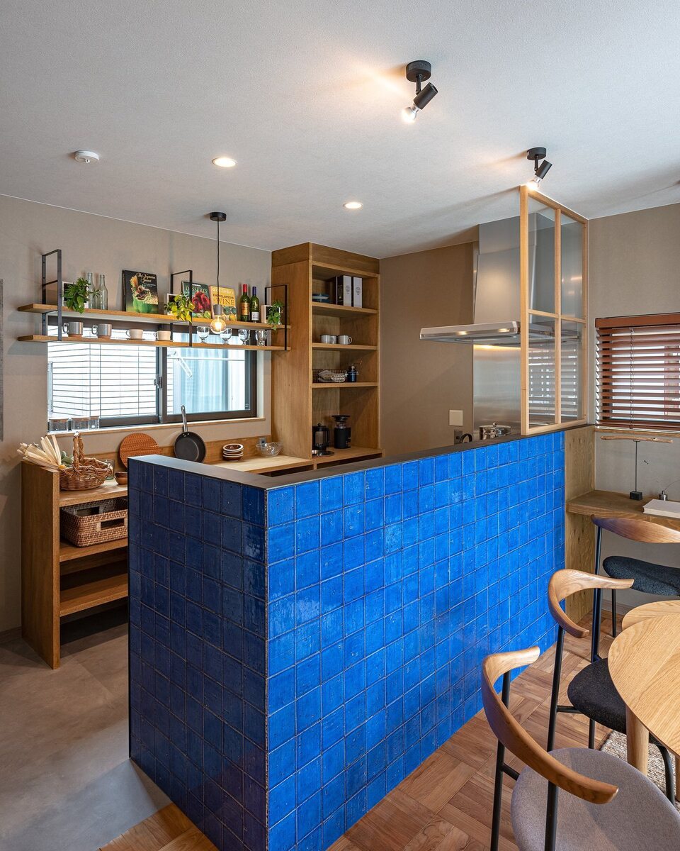 ブルーの腰壁が目を引く可愛い対面キッチン。背面収納は造作棚などオープン収納でカフェのようにおしゃれに収納。コンロ前には木枠窓を設置して機能性もデザイン性もばっちり◎